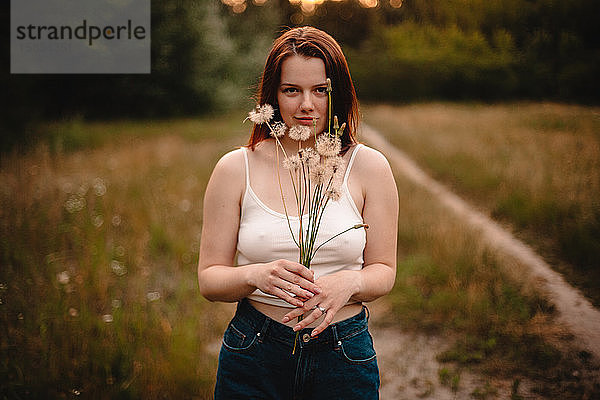 Junge Frau hält einen Strauss Löwenzahnblumen auf einer Wiese