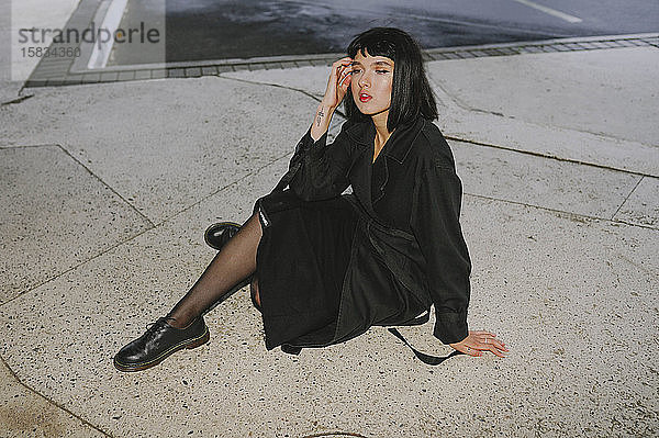Frau im schwarzen Umhang auf dem Bürgersteig sitzend