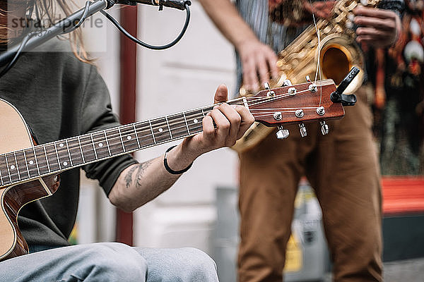 Musiker  der mitten auf der Straße vor einem Mikrofon und mit einem Saxophonisten Gitarre spielt