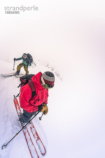 Zwei Personen beim Skitourengehen auf dem Gipfel im Nebel angekommen