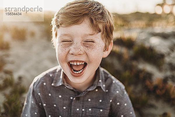 Frontansicht eines Jungen im Kindergartenalter  der während des Sonnenuntergangs am Strand lacht