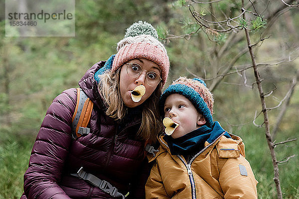 Mutter und Sohn machen beim Wandern im Winter beim Essen alberne Gesichter