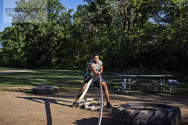 Ein Mann zieht in einem Hindernisparcours im Freien einen schweren Reifen mit einem Seil