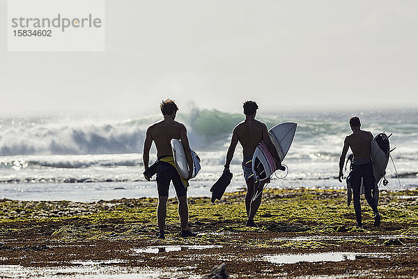 Gruppe von Männern mit Surfbrett am Strand spazieren