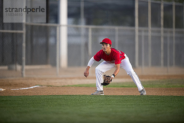 Teenager-Baseballspieler in roter Uniform bereit für einen Groundball
