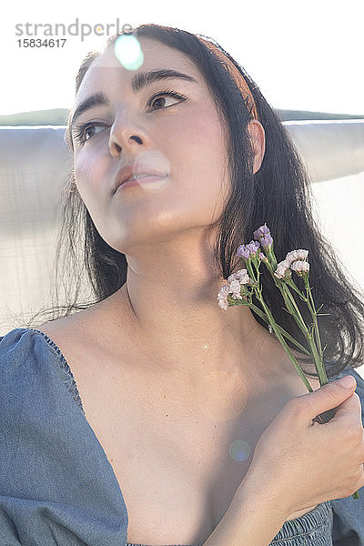 Hübsche ethnische Frau hält draußen Blumen mit einzigartiger Beleuchtung