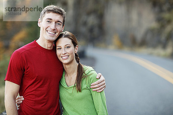 Laufendes Paar umarmt sich am Rand einer landschaftlich reizvollen Straße auf dem Land