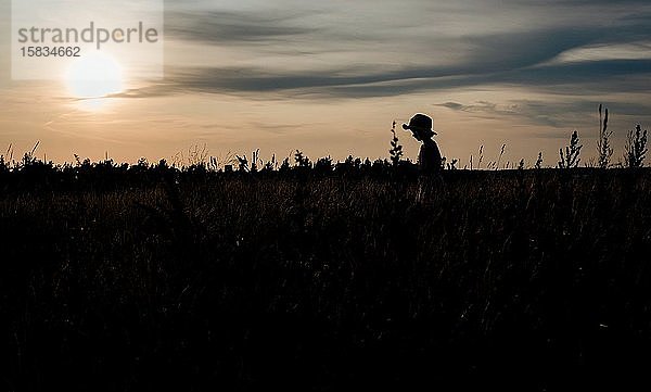 Silhouette eines Mädchens  das bei Sonnenuntergang über ein Feld läuft