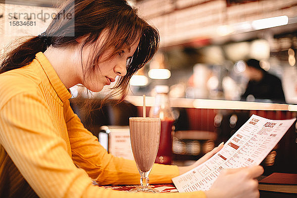 Teenagerin liest Speisekarte  während sie im Restaurant sitzt