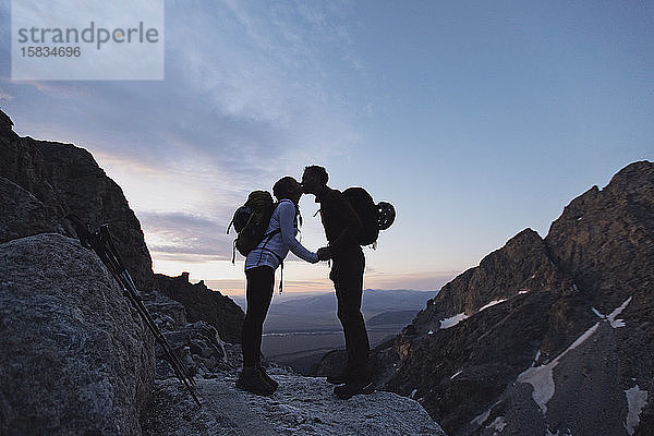 zwei Wanderer mit Rucksäcken küssen sich bei Sonnenaufgang in den Bergen  Wyoming