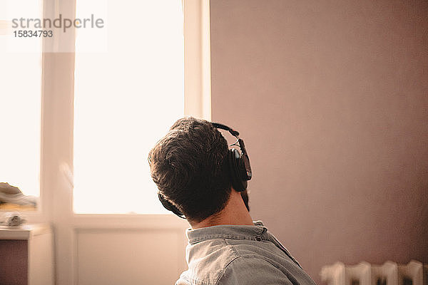 Mann schaut durch ein Fenster  während er zu Hause Musik hört und arbeitet