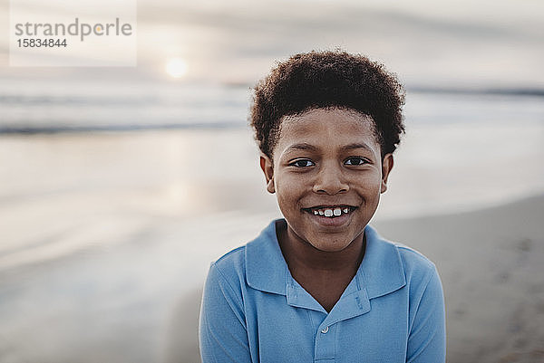 Porträt eines jungen Jungen im Schulalter  der bei Sonnenuntergang am Strand lächelt