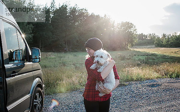 Frau  die ihren Hund trägt  während sie im Sommer in einem Wohnmobil zeltet