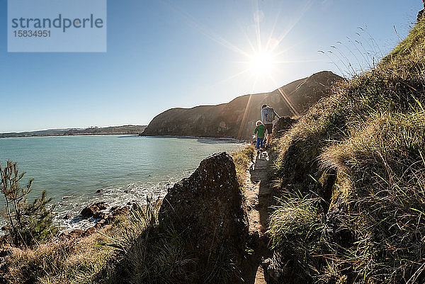 Vater und kleiner Sohn wandern auf Bergpfad über dem Meer in Neuseeland