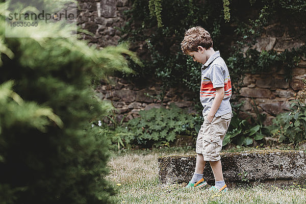 Seitenansicht eines Jungen  der im Garten gegen eine Steinmauer steht