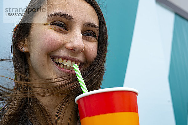 Lächelnde Frau  die auf einer Party mit einem Strohhalm Limonade trinkt.