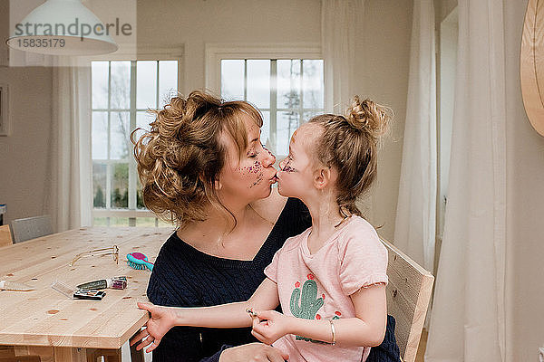 Mutter küsst Tochter  während sie zu Hause mit Make-up spielen