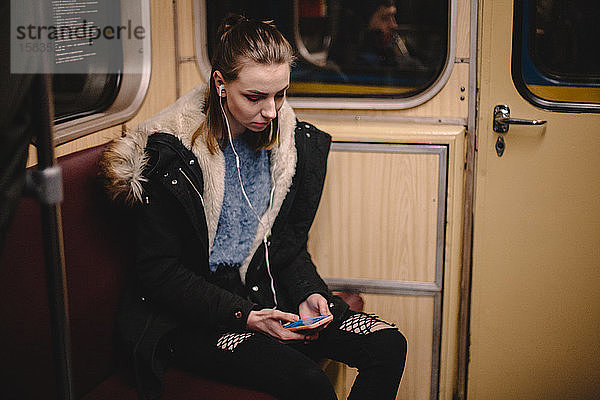 Junge Frau benutzt Smartphone während der Fahrt in der U-Bahn