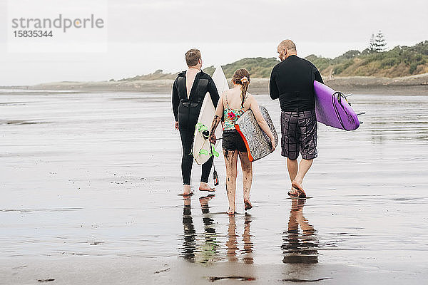 Familie beim Strandspaziergang mit Boogie und Surfbrettern