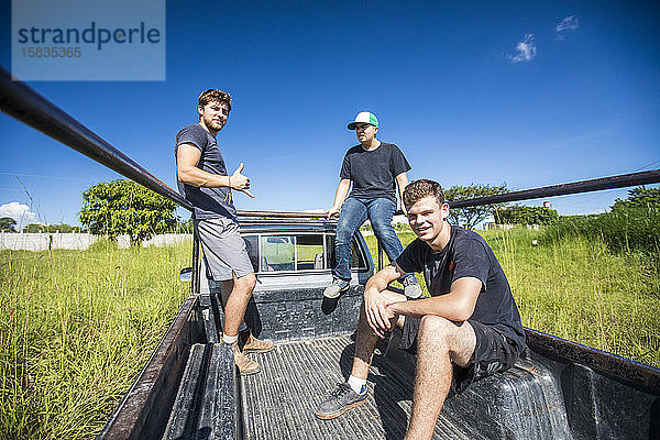 Drei junge Männer fahren hinten in einem 4x4-Lastwagen durchs Feld.