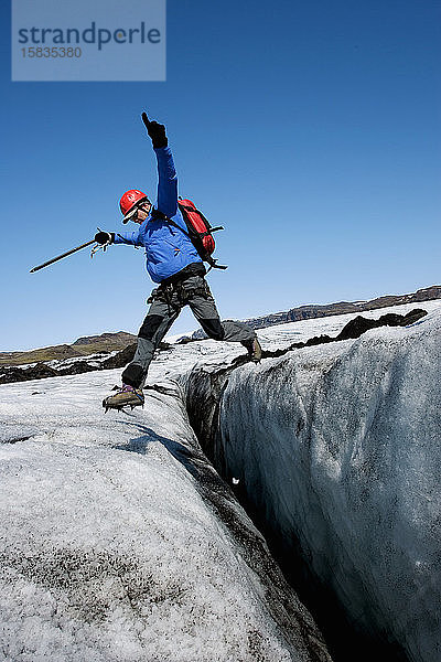 Mann springt über eine Gletscherspalte auf dem Gletscher Solheimajokull in Island