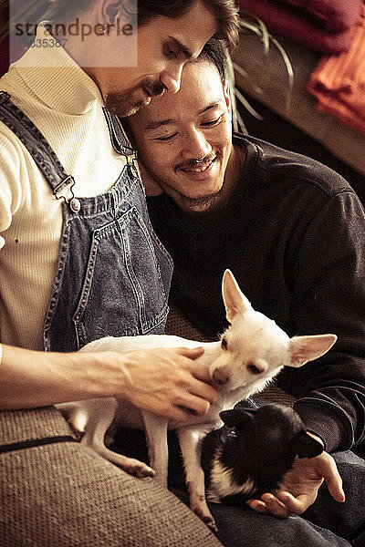 Homosexuelles  männliches  gemischtrassiges Paar kuschelt und lächelt mit Hunden zu Hause