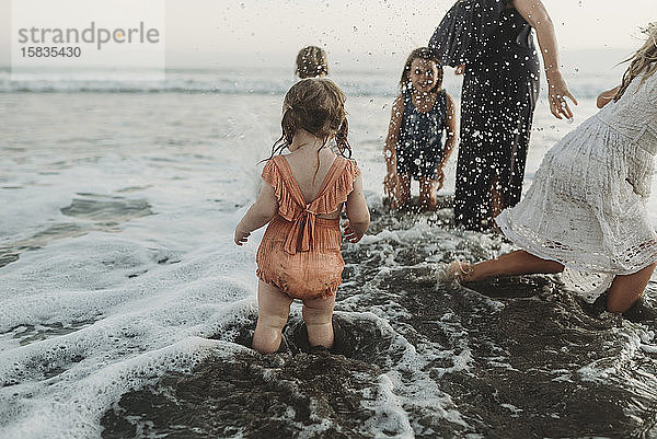 Junges Kleinkind planscht mit Schwestern und Mutter am Strand in der Abenddämmerung