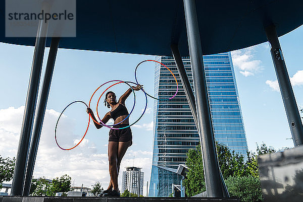 Perspektivische Ansicht einer jungen Frau  die mit vier Hula-Hoop-Reifen in der Stadt tanzt