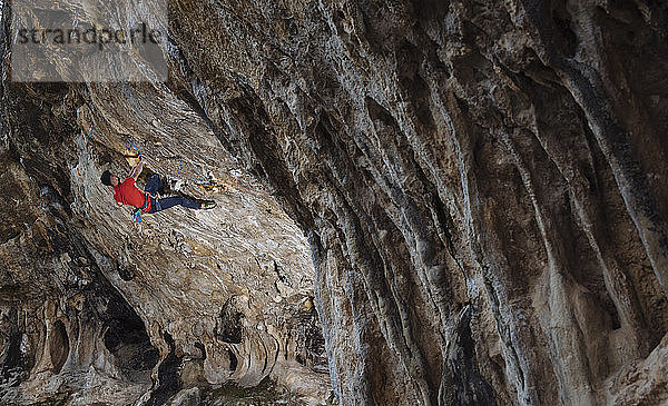 Kletterer  der eine harte Sportkletterroute in einer Höhle schickt.