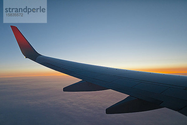 Flügel eines Flugzeugs in der Mitte der Luft bei Sonnenuntergang  das über den Planeten Erde fliegt.