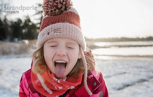 junges Mädchen  das beim Spielen draussen Schnee mit der Zunge auffängt