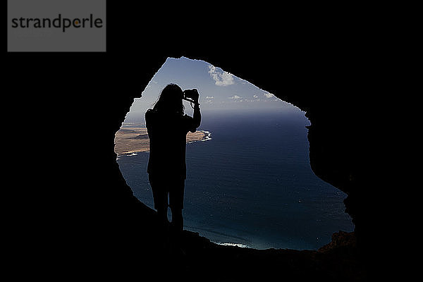 Silhouette eines Mannes  der von einer Höhle in den Klippen von Famara aus ein Foto macht.