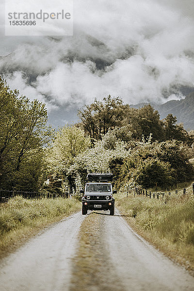 Geländewagen fährt unbefestigte  von Bergen umgebene Straße  Neuseeland