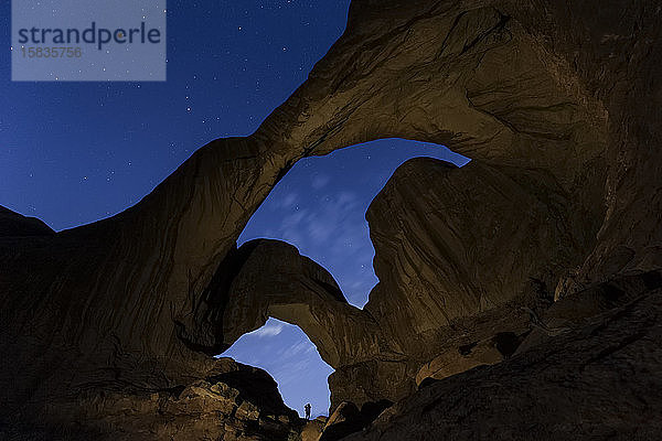 Silhouette eines Wanderers eingerahmt von Doppelbogen unter Sternenhimmel in Arches