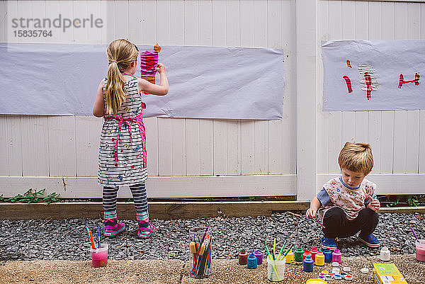 Zwei Kinder malen draußen.