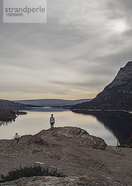 Einzelne Frau steht vor einem unberührten und ruhigen See in den Bergen