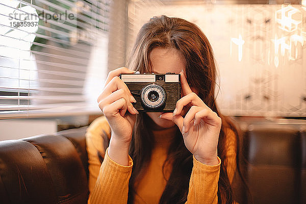 Teenager-Mädchen fotografiert mit Vintage-Kamera  während sie im Café sitzt