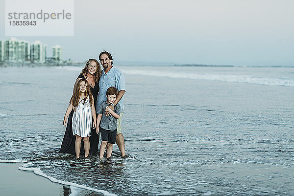 Porträt einer vierköpfigen Familie im Meer in der Abenddämmerung  die in die Kamera lächelt