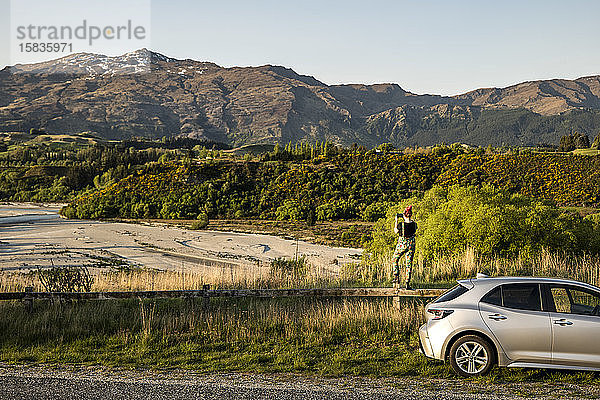 Frau und Auto mit Blick auf eine Fluss- und Berglandschaft  Neuseeland