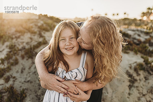 Frontansicht einer Mutter  die ihre kleine Tochter bei Sonnenuntergang am Strand umarmt