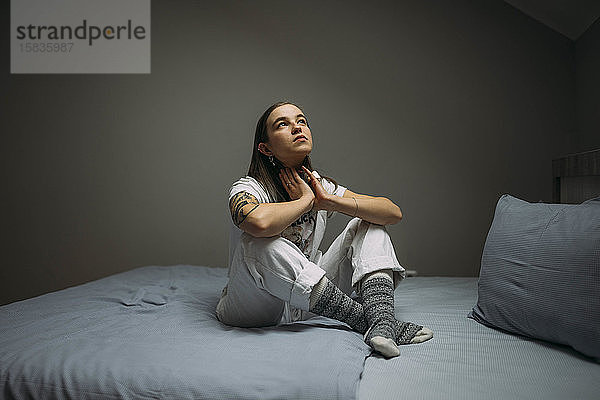 Attraktiv tätowierte junge Frau auf dem Bett sitzend