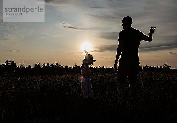 Silhouette eines Vaters und einer Tochter  die draußen bei Sonnenuntergang zusammen spielen