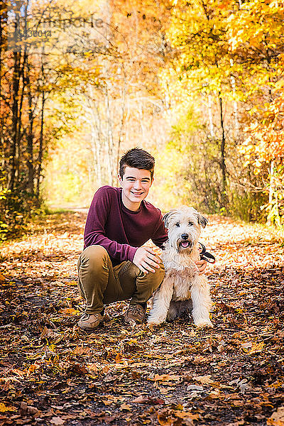 Teenagerjunge mit Pelzhund auf belaubter Fährte im Wald am Herbsttag.