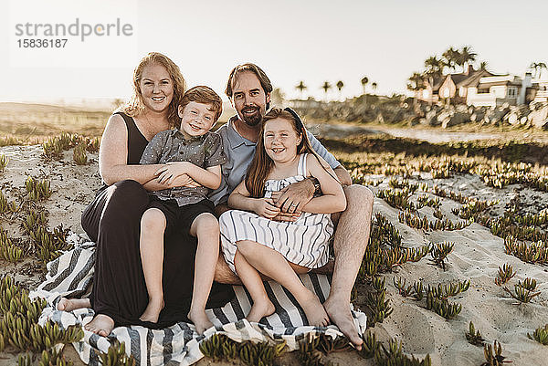 Porträt einer vierköpfigen Familie  die bei Sonnenuntergang auf einer Decke am Strand sitzt