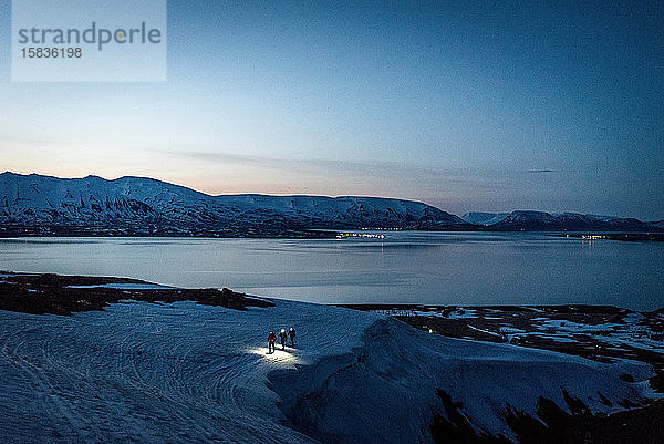 Eine Gruppe von 3 Personen fährt bei Sonnenaufgang Ski  dahinter Meer und Berge