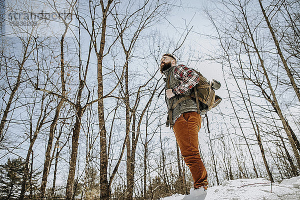 Mann mit Flanell  Bart und Rucksack steht im Winter im Schnee in den Wäldern