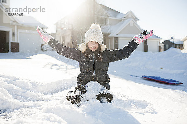 Mädchen im Alter von 10-12 Jahren amüsiert sich im Schnee vor dem Haus
