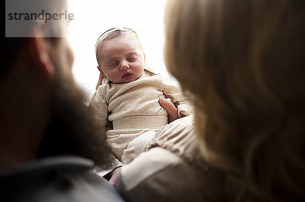 Abwärtsblick zwischen Mutter und Vater eines neugeborenen Mädchens im Schlaf