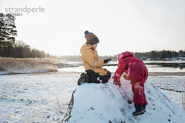 Geschwister spielen im Winter gemeinsam an der Ostsee im Schnee