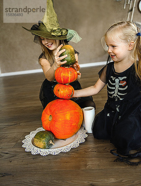 Zwei Schwestern zu Halloween in Skelettkostümen mit Kürbissen gekleidet